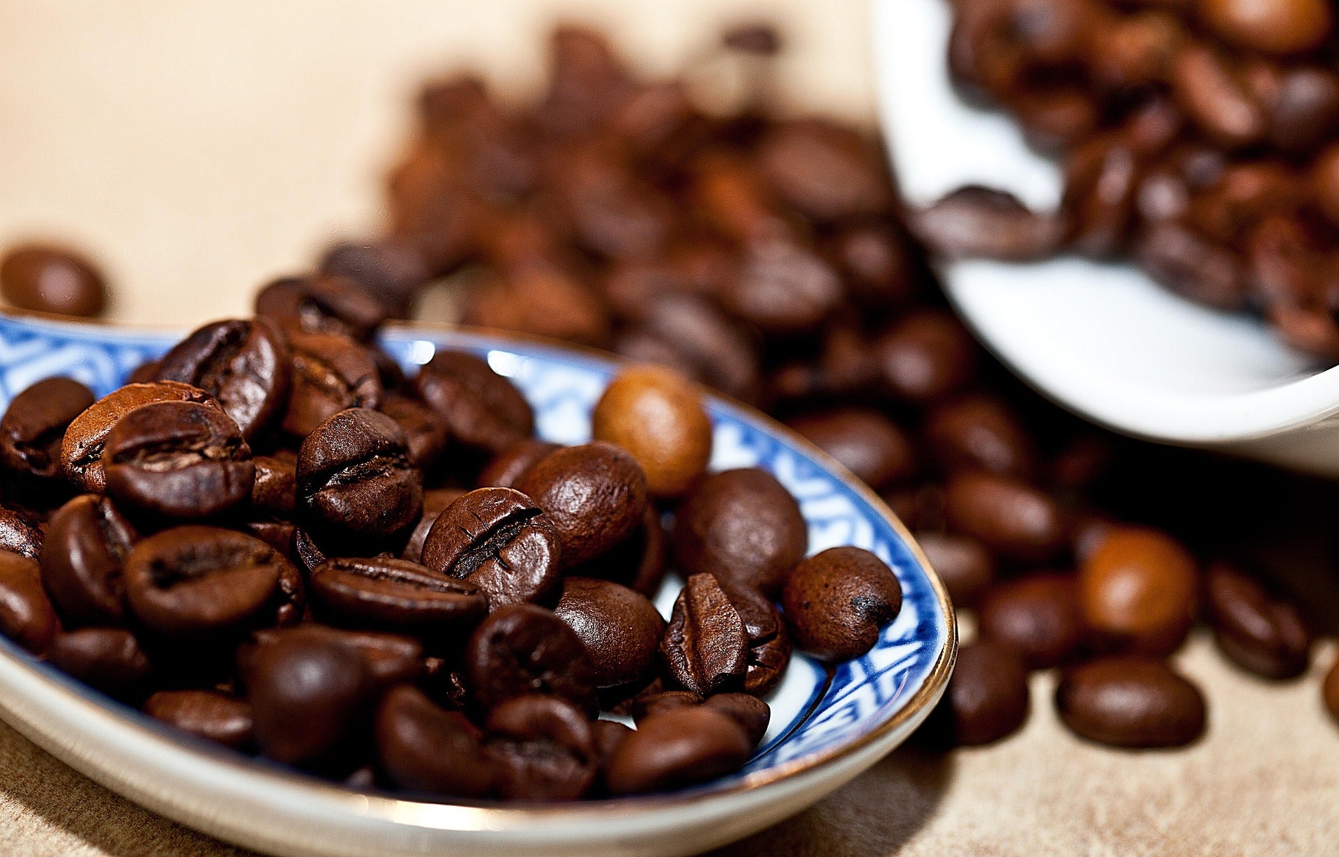 Dark roasted robusta beans spilling from a blue patterned cup